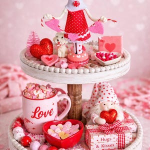 May include: A two-tiered Valentine's Day display with a wooden doll, heart-shaped candies, and a mug that says "Love." The top tier has a doll, heart-shaped decorations, and a small dog figurine. The bottom tier has a mug, heart-shaped candies, and a gift box.