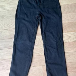 May include: Dark blue denim jeans with a classic five-pocket design. The jeans have a high waist and a straight leg cut. The fabric appears to be a medium-weight denim. The jeans are laid flat on a light wood-grain surface.