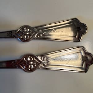 May include: Two silver spoons with ornate handles. The spoons are engraved with the name "Mary".