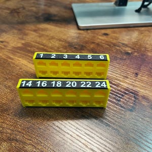 May include: Two bright yellow plastic network patch panel port organizers. The top unit features black labels numbered 1 through 6, while the bottom unit features black labels numbered 14, 16, 18, 20, 22, and 24. Each unit has six RJ45 ports.