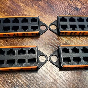 May include: Four black and orange network patch panels with multiple RJ45 ports. Each panel has a series of numbered ports, and a loop on each end. The panels are arranged on a wooden surface.