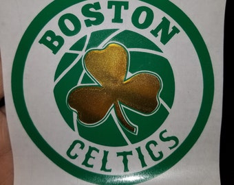 May include: A green and white circular sticker with the words "BOSTON CELTICS" in a white font. A gold shamrock is in the center of the sticker.