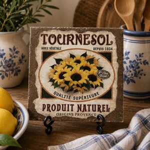 Könnte beinhalten: Eine quadratische Dekofliese mit einer zentralen Abbildung gelber Sonnenblumen. Der Text lautet Tournesol, Huile Végétale, Depuis 1934, Qualité Supérieure, Produit Naturel, Origine Provence und 1er Choix Garanti. Die Fliese hat einen abgenutzten Rand.