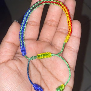 May include: A multi-colored friendship bracelet with green, blue, yellow, and red threads. The bracelet is tied in a knot at the ends.