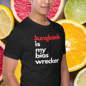 May include: A black t-shirt with white text that reads "Jungkook is my bias wrecker" in red letters. The person wearing the shirt is standing in front of a background of citrus fruit slices.