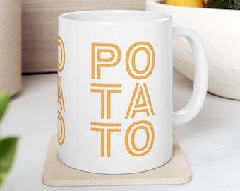 Könnte beinhalten: Weiße Keramiktasse mit einem goldenen Umriss des Wortes "POTATO" auf der Vorderseite. Die Tasse steht auf einem beigefarbenen Untersetzer.