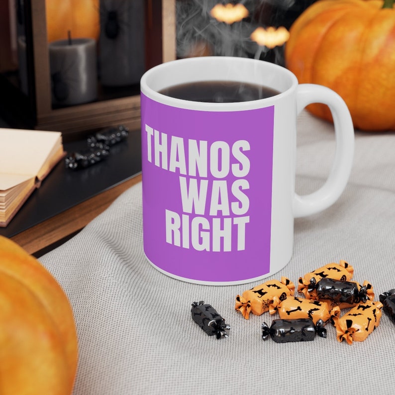 K&ouml;nnte beinhalten: Eine lila Kaffeetasse mit dem Text "THANOS WAS RIGHT" in wei&szlig;en Buchstaben. Die Tasse steht auf einer grauen Stoffoberfl&auml;che mit orangefarbenen und schwarzen S&uuml;&szlig;igkeiten.