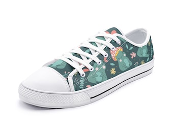 Op de afbeelding: Witte canvas lage sneakers met een groene achtergrond en een herhalend patroon van cartoon kikkers die paddenstoelhoeden dragen.