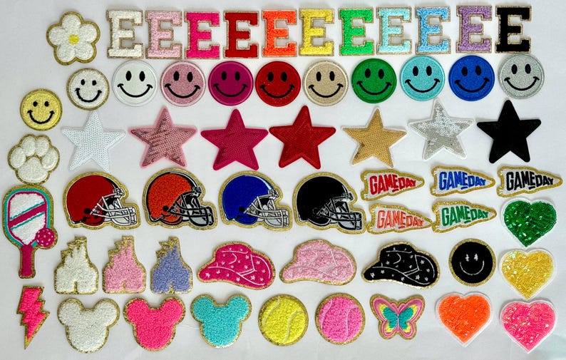 May include: A collection of iron-on patches featuring various designs, including letters, stars, smiley faces, game day pennants, helmets, and more. The patches are all in different colours and styles.