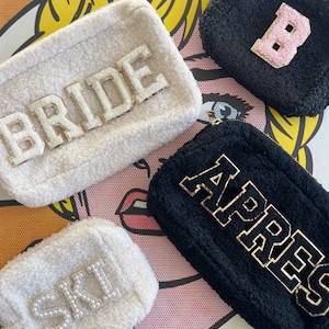 Può includere: Quattro pochette rettangolari e soffici in crema e nero. Le pochette color crema hanno le parole "BRIDE" e "SKI" in lettere dorate e perlate. Le pochette nere hanno le lettere "B" e "APRES" in lettere dorate.