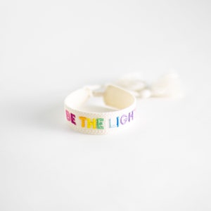 May include: White woven bracelet with a rainbow colored embroidered message that reads "BE THE LIGHT".