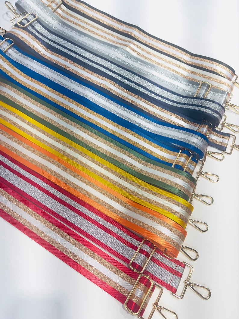 May include: A collection of colorful striped fabric straps with gold glitter accents. The straps have gold metal clasps and are arranged in a stack.
