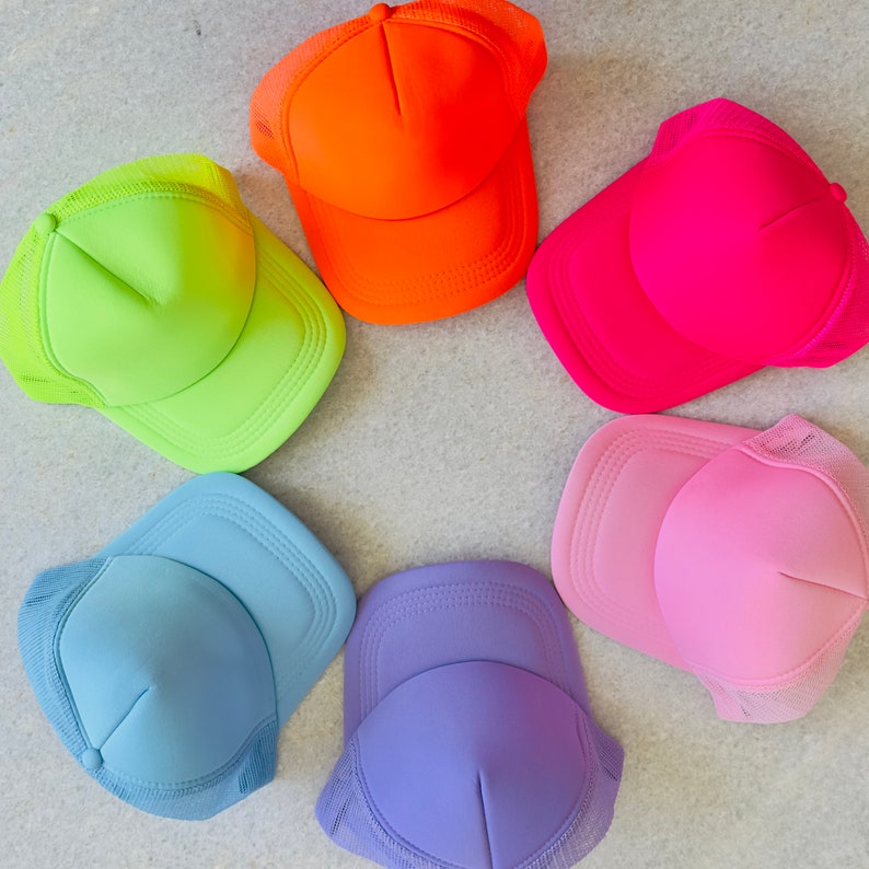 May include: Six neon coloured trucker hats arranged in a circle. The hats are in the colours: orange, green, pink, light blue, purple, and light pink.
