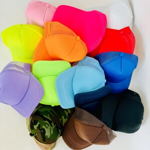 May include: A collection of 12 colourful trucker hats in various colours, including neon green, pink, red, blue, light blue, brown, black, camouflage, and orange. The hats are made of a mesh material with a solid front panel.