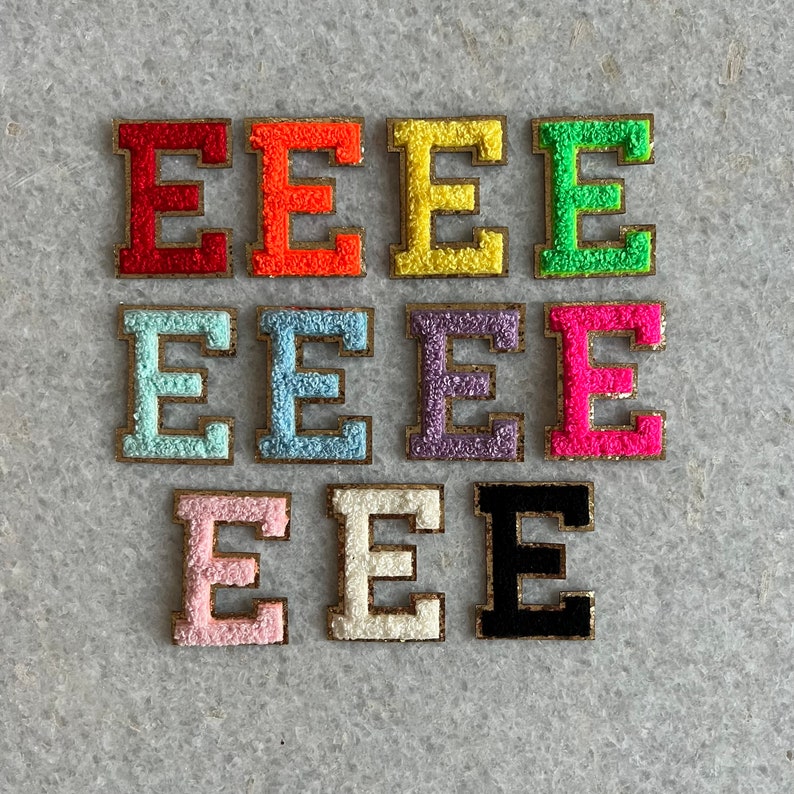 May include: Ten felt letter patches in various colours, each featuring the letter "E" in a gold outline. The colours include red, orange, yellow, green, light blue, dark blue, purple, pink, white, and black.