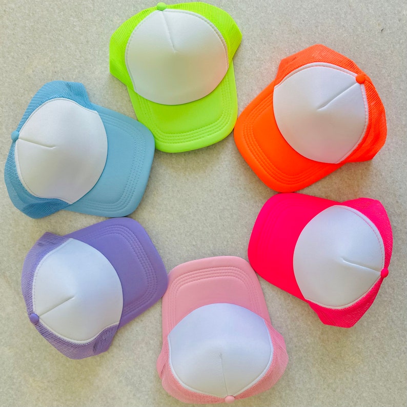 May include: Six blank trucker hats arranged in a circle. The hats are in the following colours: light blue, light green, orange, pink, purple, and hot pink.