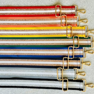 May include: A set of eight striped fabric straps with gold hardware. The straps are in various colors, including red, orange, yellow, green, blue, and gray. Each strap has a gold buckle and a gold clip.
