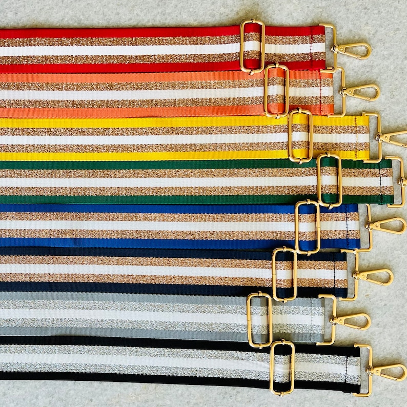 May include: A set of eight striped fabric straps with gold hardware. The straps are in various colors, including red, orange, yellow, green, blue, and gray. Each strap has a gold buckle and a gold clip.