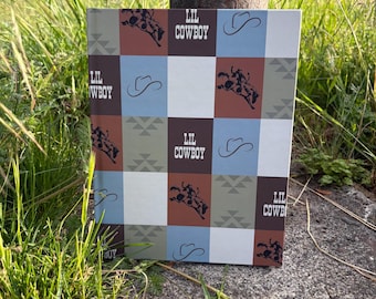 May include: A square box with a patchwork design featuring cowboy-themed graphics. The design includes images of a cowboy riding a bull, cowboy hats, and geometric patterns in brown, blue, and white squares. The words "LIL COWBOY" are printed on the box.