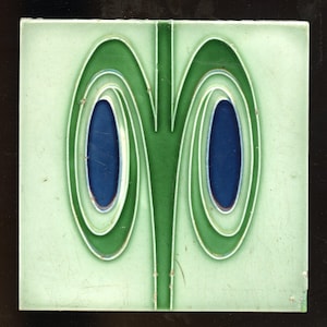 May include: A green and blue ceramic tile with a stylized design of two overlapping ovals with a central stem.