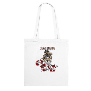 Op de afbeelding: Witte tote bag met bruine tekst die "DEAD INSIDE" zegt en een schedel met luipaardprint haar en zonnebril omringd door rode rozen.