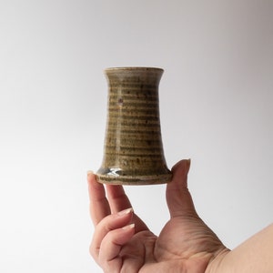 May include: A small, brown ceramic vase with a flared base and a narrow opening. The vase has a striped pattern and a glossy finish.