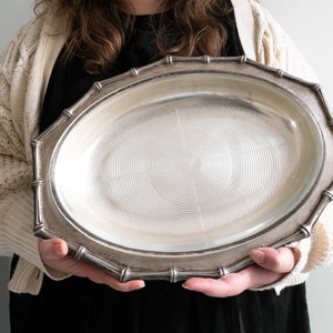 May include: A silver serving platter with a bamboo-style rim. The platter has a circular, concentric pattern on the bottom.
