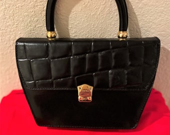 May include: A black leather handbag with a gold-tone handle and clasp. The bag has a quilted texture.
