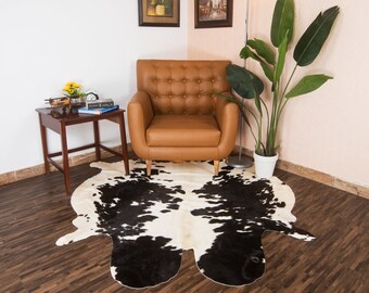 Puede incluir: Una alfombra de piel de vaca en blanco y negro con un sillón de cuero marrón y una planta en maceta en el fondo.