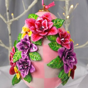 Könnte beinhalten: Rosa-weiß kariertes Osterei-Ornament, verziert mit rosa, lila und gelben Blumen und grünen Blättern.