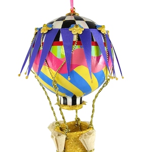 May include: A colorful hot air balloon ornament with a checkered top, blue and yellow stripes, and a pink and green band. The balloon has a gold basket and a purple and gold trim.
