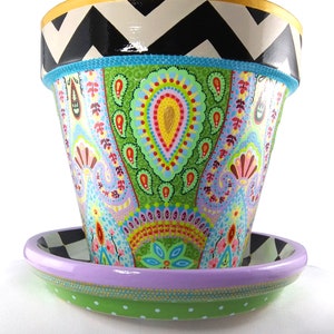 May include: A hand-painted ceramic planter with a green, pink and blue paisley design. The planter has a black and white chevron pattern around the top rim and a matching saucer with a green and white polka dot pattern.