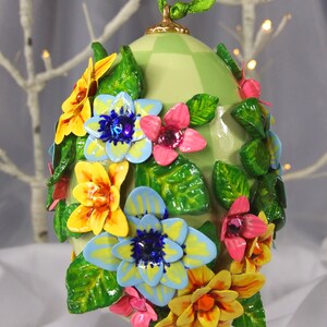 May include: A green and white chequered Easter egg ornament decorated with colourful flowers and leaves. The flowers are made of fabric and have a 3D effect.