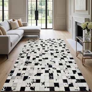 Puede incluir: Una alfombra rectangular con un diseño de patchwork en blanco y negro. La alfombra está hecha de cuadrados de piel de vaca, creando un patrón de tablero de ajedrez. La alfombra está colocada sobre un suelo de madera en un salón.