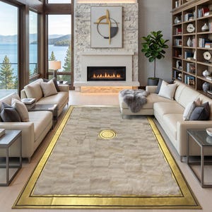 Op de afbeelding: Een rechthoekig vloerkleed met een getextureerd, lichtgekleurd patchwork-oppervlak met een brede, metallic gouden rand en een gecentreerde ronde gouden inleg, geplaatst op een lichte houten vloer in een woonkamer met twee witte banken.