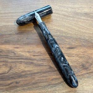 May include: A white ceramic mug with a black handle and the text "But First, Coffee" in a black, handwritten-style font. The mug is on a white surface.