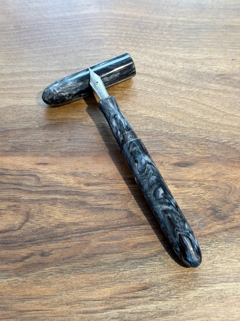 May include: A white ceramic mug with a black handle and the text "But First, Coffee" in a black, handwritten-style font. The mug is on a white surface.