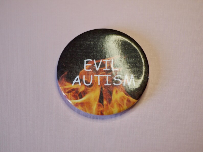 以下が含まれることがあります： 炎を背景に「EVIL AUTISM」の文字が白で書かれた丸いボタン。オレンジと黄色の炎のデザインが施された、黒とグレーの背景です。