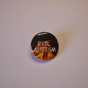 以下が含まれることがあります： 白い文字で「EVIL AUTISM」と書かれた丸いボタン。ボタンの背景には、オレンジと黄色の炎の燃えるようなデザインが施されています。ボタンは黒色で光沢があります。