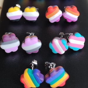 May include: A set of 10 colorful flower-shaped earrings with different pride flag designs. The earrings are made of polymer clay and have silver posts.