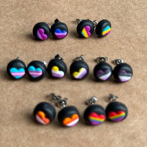 May include: A set of 10 black stud earrings with different colored hearts representing various pride flags. The flags include bisexual, pansexual, transgender, non-binary, lesbian, gay, and asexual.