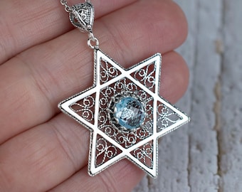 Pode incluir: Um pingente de prata em forma de Estrela de David com uma gema azul no centro. O pingente está em uma corrente de prata.