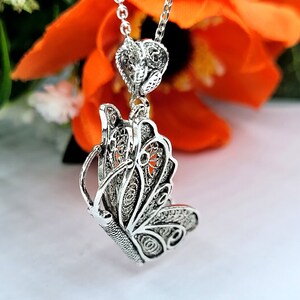 Pode incluir: Um colar de prata com um pingente de borboleta com um delicado design de filigrana. O pingente &eacute; pendurado em uma corrente de prata e tem um charme em forma de cora&ccedil;&atilde;o.