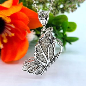 Pode incluir: Colar com pingente de borboleta em filigrana de prata, com um design delicado. O pingente apresenta uma borboleta detalhada com asas intrincadas e uma pequena corrente presa ao topo. O colar &eacute; feito de prata e tem uma corrente de prata.