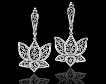 May include: A pair of silver filigree earrings with a lotus flower design. The earrings are dangling and have a delicate, intricate pattern.