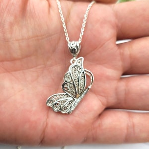 Pode incluir: Um colar com um pingente de borboleta de filigrana de prata. A borboleta &eacute; detalhada e intrincada, com uma corrente delicada.