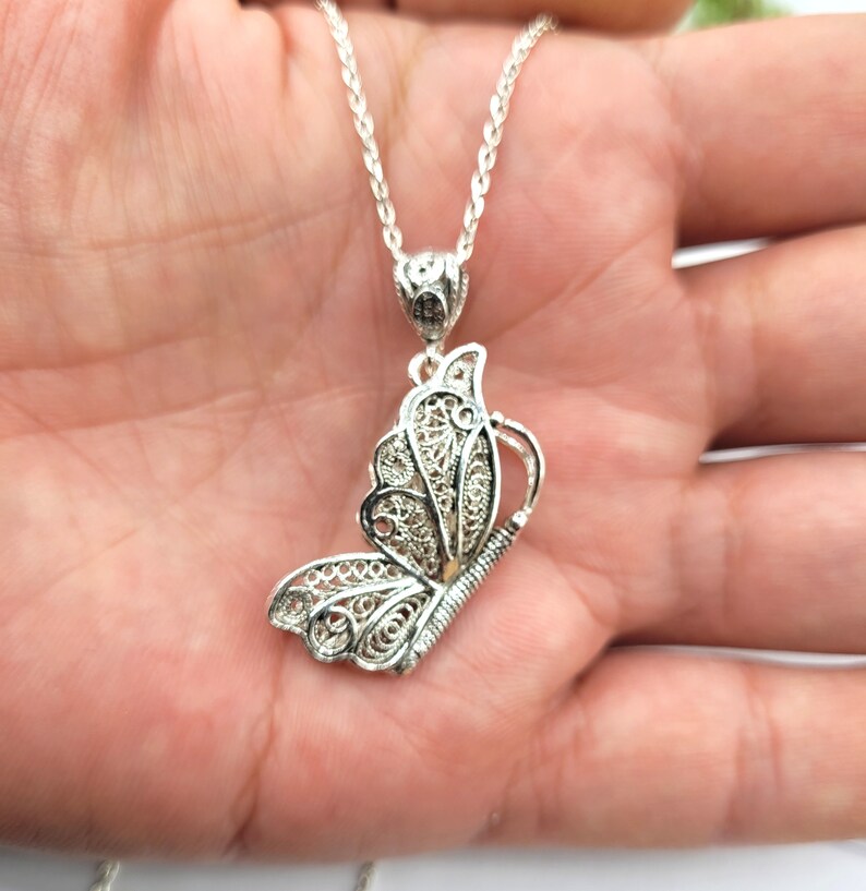 Pode incluir: Um colar com um pingente de borboleta de filigrana de prata. A borboleta &eacute; detalhada e intrincada, com uma corrente delicada.