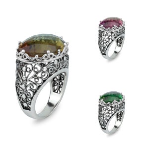 May include: Three silver filigree rings with different coloured gemstones. The rings feature a detailed filigree design and a large oval-shaped gemstone in the centre. The gemstones are green, purple, and brown.