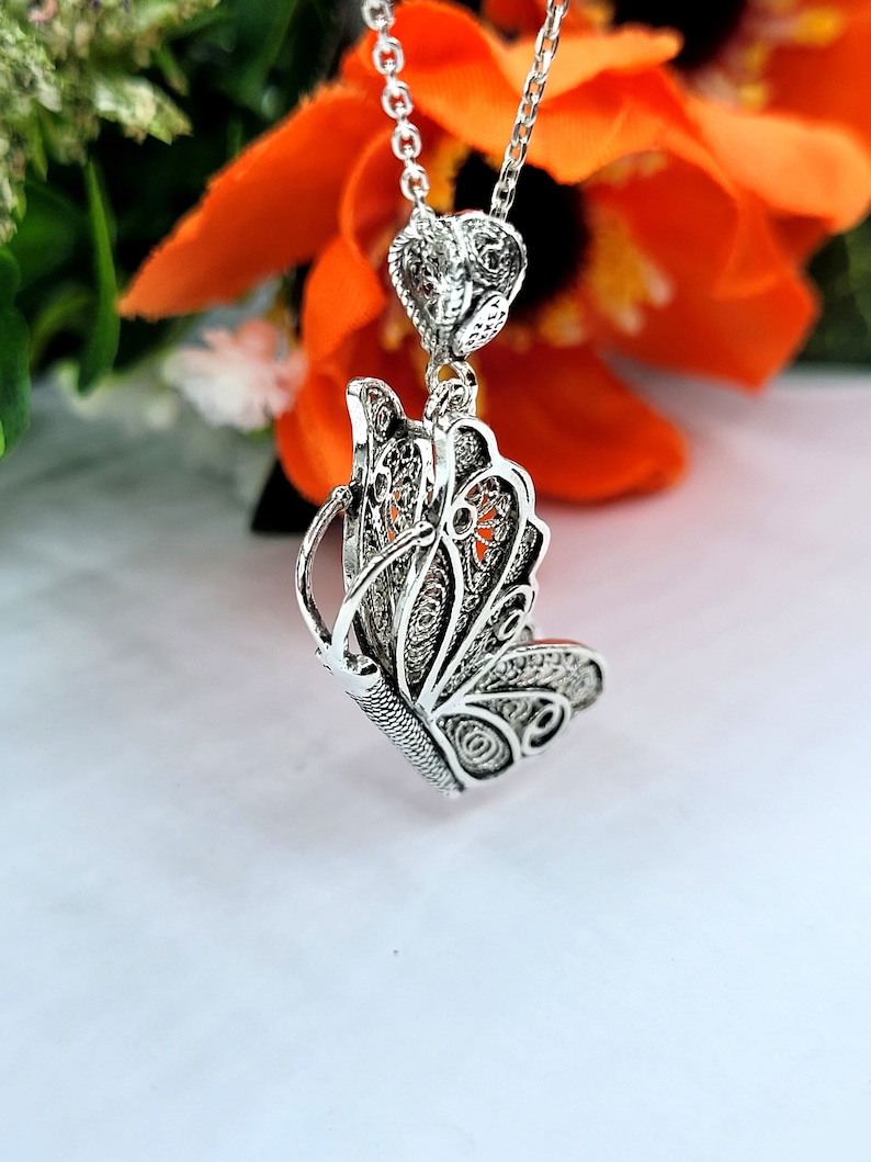 Pode incluir: Um colar de prata com um pingente de borboleta com um delicado design de filigrana. O pingente &eacute; pendurado em uma corrente de prata e tem um charme em forma de cora&ccedil;&atilde;o.