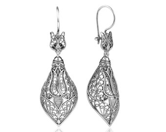 May include: Silver filigree earrings with a teardrop shape and a floral design. The earrings have a hook closure.